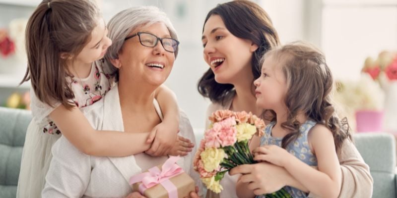 A grandmother and her daugther and grandchildren with a gift and flowers