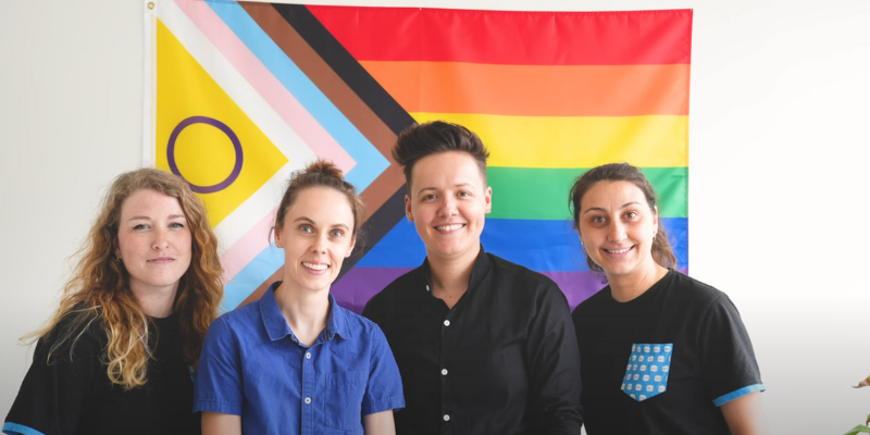 Portrait de 4 femmes devant un drapeau LQGBT+